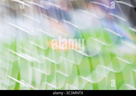 Verschwommenes Bild eines Fußballnetzes unter hellem Sonnenlicht, mit grünem Gras im Hintergrund. Das weiße Netz und das lebendige Feld sorgen für eine dynamische Atmosphäre Stockfoto