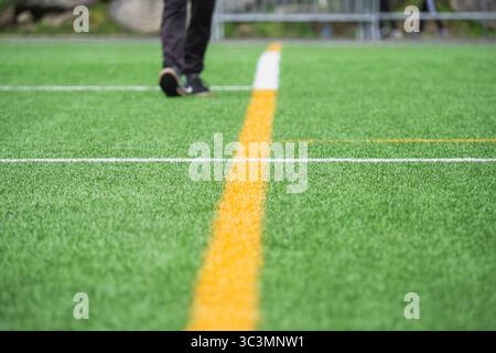 Abgeschnittene, nicht erkennbare Person, die auf einem leeren Sportplatz auf lebhaftem grünem Gras mit gelben und weißen Linien läuft. Die Szene spielt an einem sonnigen Tag, wi Stockfoto