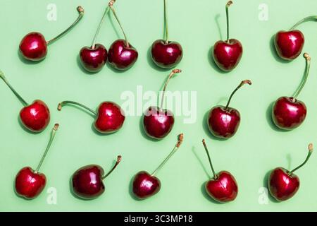 Draufsicht auf frische Kirschen, die in einem Muster auf einem glatten grünen Hintergrund angeordnet sind. Das leuchtende Rot der Kirschen bildet einen schönen Kontrast zum Grün, c Stockfoto