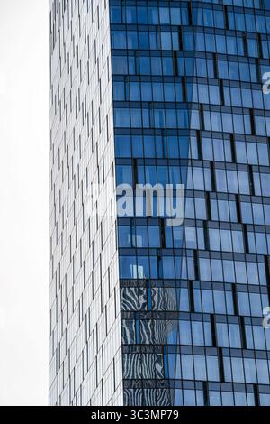 Das Bild zeigt einen modernen Wolkenkratzer mit einer eleganten Glas- und Stahlfassade, die die städtische Umgebung widerspiegelt. Die Architektur verkörpert zeitgenössisches Stockfoto