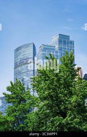 Ein lebhafter Blick auf die Stadt mit moderner Architektur mit eleganten Glashochhäusern, die bis in den klaren blauen Himmel reichen, eingerahmt von üppigen grünen Bäumen im Fo Stockfoto