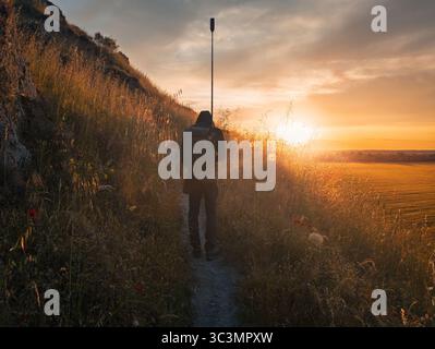 Ein Wanderer spaziert auf einem schmalen Pfad, umgeben von üppigem Gras bei Sonnenuntergang über den Feldern in Ontigola, Toledo, Spanien, und schafft eine ruhige und malerische Atmosphäre Stockfoto