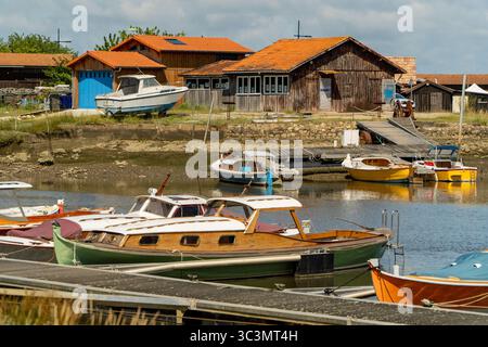 Traditionelle Holzboote ruhen sanft in einem malerischen Hafen in Arcachon Bay aus, umgeben von ruhigem Wasser und rustikalen Bootshäusern, wodurch ein malerisches coa entsteht Stockfoto