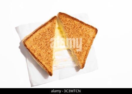 Ein köstliches Sandwich mit gegrilltem Käse liegt auf weißem Pergamentpapier auf einem sauberen, weißen Hintergrund und wird aufgespalten, um perfekt geschmolzenen Käse zu zeigen Stockfoto