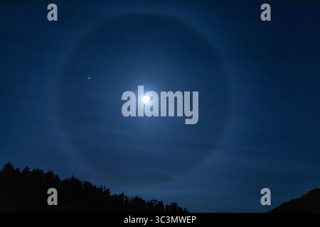 Der Vollmond scheint hell am herbstlichen Nachthimmel über den Pyrenäen und schafft eine ruhige und mystische Szene. Silhouettenbäume stehen gegen das Moo Stockfoto