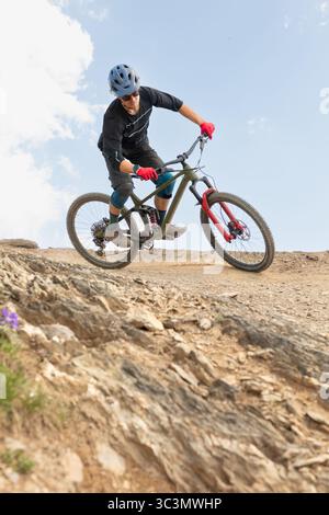 Von unten fährt ein Mann in Schutzkleidung mit dem Mountainbike in den Alpen bergab. Mitten im Geschehen, mit der Kraft und Können auf dem robusten tr Stockfoto