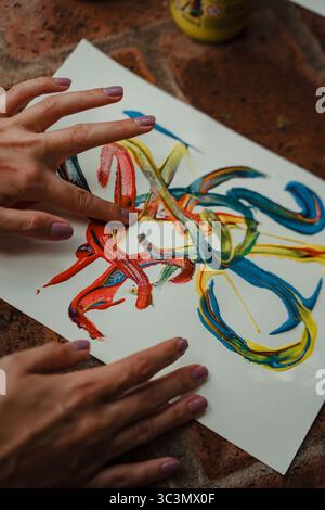 Eine Nahaufnahme von Händen, die lebendige Farben auf Papier führen und ein abstraktes Kunstwerk schaffen. Die dynamischen Konturen fließen in lebendigen Farben und betonen Kreativität und Stockfoto