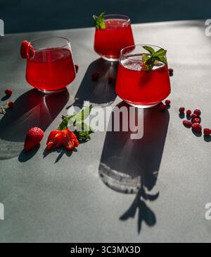 Von oben sitzen drei Gläser erfrischenden Hibiskus und Erdbeertee auf einem Tisch, beleuchtet von direktem Sonnenlicht. Garniert mit Minze, dieses kalte Rot Stockfoto