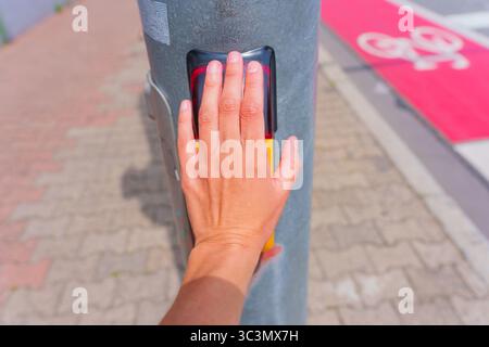 Nahaufnahme einer Hand, die einen hellgelben Fußgänger-Signalknopf an einem Metallmast drückt. Stockfoto