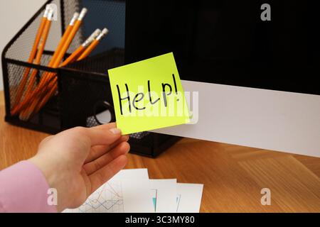 Frau, die Papiernotiz mit Worthilfe vom Monitor am Arbeitsplatz nimmt, Nahaufnahme Stockfoto