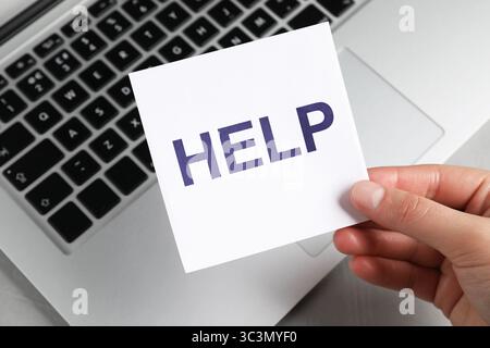 Frau, die einen Papierbrief hält, mit Worthilfe über dem Laptop, Nahaufnahme Stockfoto