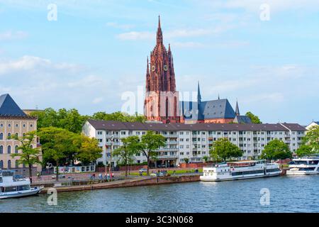 Frankfurt, Deutschland - 10. Juni 2025: Farbenfroher Blick auf eine historische Kirche und Wohngebäude entlang des Flusses in Frankfurt, Deutschland, unter einem hellen Licht Stockfoto