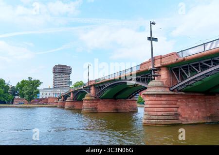 Frankfurt, Deutschland - 10. Juni 2025: Architektonischer Blick auf eine historische Brücke über einen Fluss in Frankfurt, mit urbanen Gebäuden und Lu Stockfoto