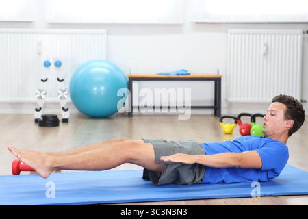 Junger Mann, blaues Hemd auf Fitnessmatte, Beine in der Luft Stockfoto