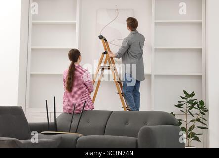 Paare, die zu Hause mit einer Leiter Malerei an die Wand legen Stockfoto