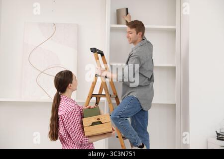 Ein Paar, das Bücher zu Hause mit einer Leiter in die Regale legt Stockfoto