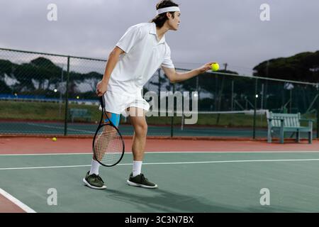 Tennisspieler, der auf dem Hartplatz steht und das Servieren vorbereitet, Ball hält und Schläger in der Nähe des Zauns packt Stockfoto