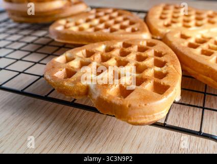 Detaillierte Nahaufnahme einer frisch gebackenen, goldbraunen Waffel in Herzform mit knuspriger Textur auf einem Kühlregal Stockfoto