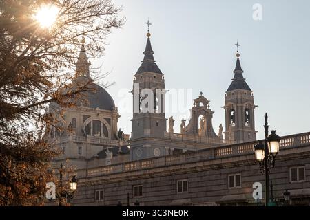 Madrid, Spanien. Zwei Glockentürme und zentrale Kuppel der Kathedrale von Almudena, beleuchtet von der Wintersonne bei Sonnenaufgang, gesehen gegen das Licht. Neoklassizistische Fassade Stockfoto