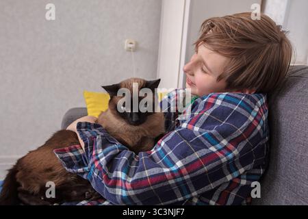 Der Junge kuschelt eine Katze auf einer gemütlichen Couch. Stockfoto