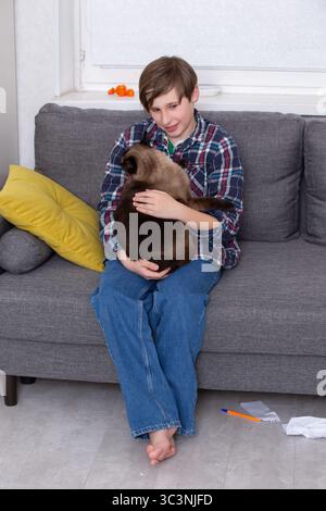Ein Junge sitzt auf einer Couch und hält eine Katze in den Armen. Stockfoto