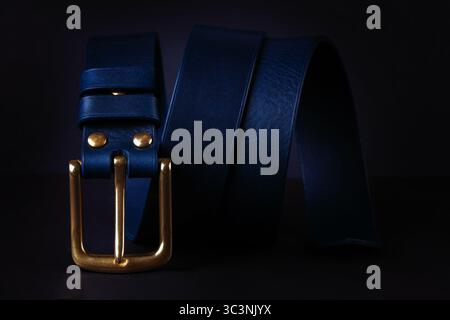 Ein blauer Gürtel mit goldener Schnalle ist auf schwarzem Hintergrund zu sehen. Der Gürtel besteht aus Leder und hat eine goldene Schnalle Stockfoto