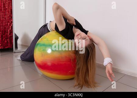 Eine junge Frau lehnt sich auf einen lebendigen Trainingsball zurück, während sie in einem gut beleuchteten Studio eine Stretchroutine durchführt. Sie konzentriert sich auf Balance und Flexibilität Stockfoto