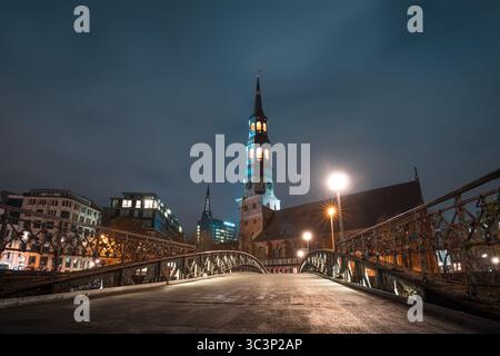 Katharinenkirche in Hamburg bei Nacht mit beleuchtetem Turm und bewölktem Himmel entlang einer Brückenperspektive Stockfoto
