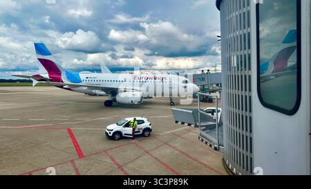 Eurowings Airbus A320 (D-AEXT) am Flughafen Düsseldorf (DUS) mit Servicefahrzeug und Personal auf dem Asphalt unter teilweise bewölktem Himmel. Stockfoto
