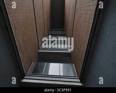 Flacher Blick auf einen schmalen Durchgang zwischen zwei Backsteingebäuden mit einer Reihe von Balkonen mit Glasgeländern. Die Wände haben einen Stockfoto