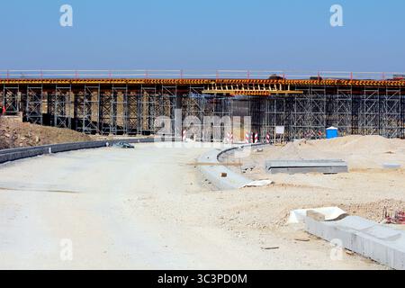 Eine große Brücke wird mit umfangreichen Gerüsten gebaut, darunter Erdarbeiten, Straßenbettvorbereitungen und sichtbare Baumaterialien Stockfoto