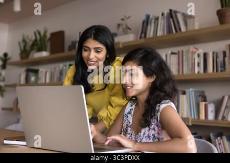 Zwei attraktive indische Arbeitskollegen, die im modernen Büro einen Laptop verwenden Stockfoto