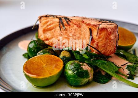 Köstlich gegrilltes Lachsfilet mit frischem Rosenkohl und Limettenscheiben, garniert mit einer cremigen Sauce für einen einladenden kulinarischen Genuss Stockfoto