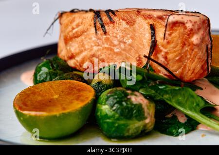 Ein wunderschön überzogenes Gericht mit professionell gegrilltem Lachsfilet, serviert mit einem Gemisch aus frischem Gemüse und würziger Limette, perfekt für ein gesundes Essen Stockfoto