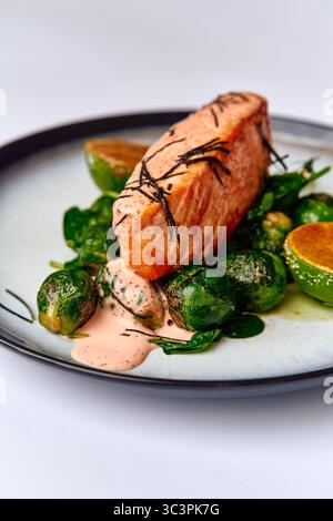 Köstlich gegrilltes Lachsfilet mit saisonalen Rosenkohl, Spinat, Limettensegmenten und einem cremigen Dressing auf einem stilvollen Teller Stockfoto