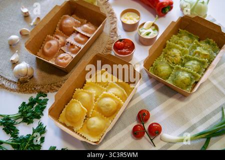 Eine köstliche Auswahl an frisch zubereiteten Ravioli-Sorten, serviert in Kartonschachteln mit bunten Zutaten und Garnelen auf einem rustikalen Tisch Stockfoto