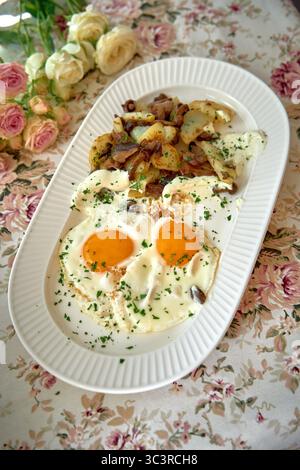 Köstlich gefertigter Frühstücksteller mit Eiern von der Sonnenseite, aromatischen Kartoffeln und herzhaftem gehacktem Gemüse, garniert mit frischen Kräutern Stockfoto