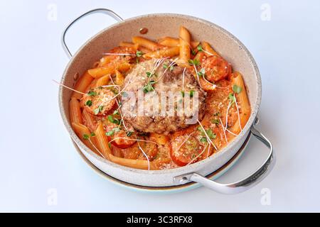 Köstlich gebackenes Pasta-Gericht mit knusprigem Hähnchenkotelett, belegt mit frischen Tomaten und garniert mit Microgreens in einer stilvollen Servierpfanne Stockfoto