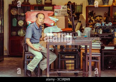 Hongkong, China, 23. Juli 2017 : Ein chinesischer Mann mittleren Alters saß und aß mit Essstäbchen auf einem Holztisch in seinem Geschäft Stockfoto