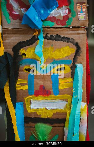 Kunst für Kinder. Farbenfrohe, bemalte Maske auf Karton mit dynamischen Texturen und kräftigen Pinselstrichen, mit Taschentuch und Federn, reflektierendem cre Stockfoto