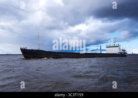 Frachtschiff bewegt sich durch Wellen unter einem trüben, bewölkten Himmel Stockfoto