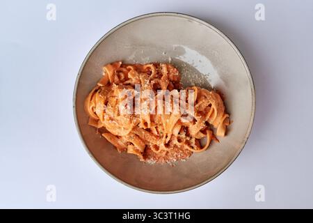 Köstliche Fettuccine-Pasta in cremiger Tomatensauce mit frischem Parmesan auf einer minimalistischen Platte vor einem einfachen weißen Hintergrund Stockfoto