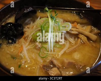 Traditionelle köstliche Ramen-Nudelsuppe mit Miso-Paste, Fleisch, Algen und Zwiebeln in einer Schüssel mit einem Holzlöffel in Japan Stockfoto