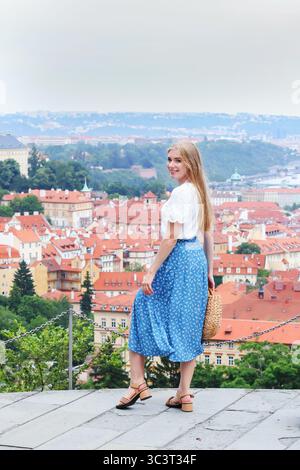 Frau im blauen Rock lächelt über Prager Dächer, Sommerreise durch Europa. Stockfoto