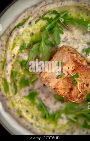 Ein Blick aus nächster Nähe auf köstliches in der Pfanne angebratenes Fischfilet, eingebettet in eine cremige Sauce mit frischen Kräutern und Microgreens für ein Gourmet-Erlebnis Stockfoto