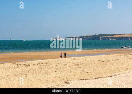 Knoll Beach, Studland, Großbritannien - 25. Juli 2025: Paar spazieren am Strand mit den Old Harry Rocks im Hintergrund. Stockfoto