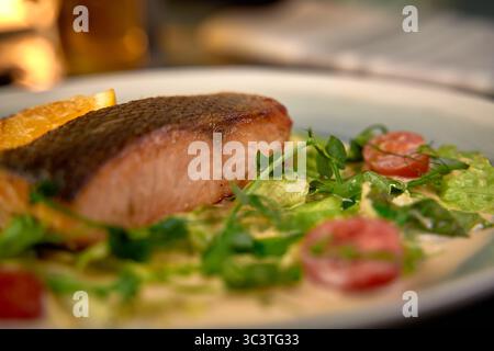 Köstlich gegrilltes Lachsfilet, serviert auf frischem Gemüse mit Kirschtomaten und Zitrusgarne in warmer Atmosphäre Stockfoto
