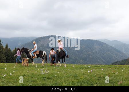 Eine Gruppe von Menschen und Pferden ist in einem Blumenfeld. Zwei reiten Pferde, während zwei andere laufen. Stockfoto