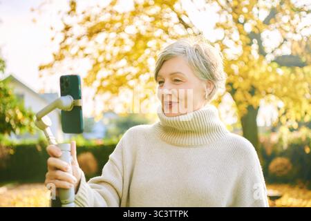 Outdoor-Porträt einer glücklichen und aktiven Reifen Frau, die sich mit Telefon, sozialen Medien und Vlogging-Konzept aufnimmt Stockfoto