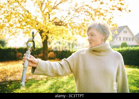 Outdoor-Porträt einer glücklichen und aktiven Reifen Frau, die sich mit Telefon, sozialen Medien und Vlogging-Konzept aufnimmt Stockfoto